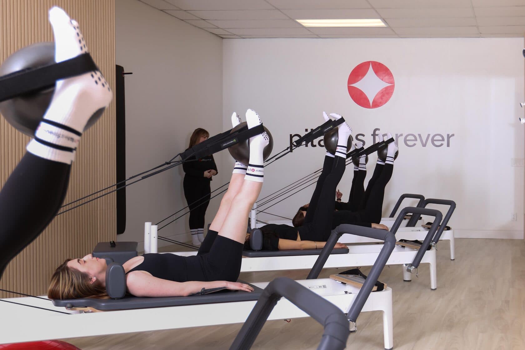 Group reformer class doing leg exercises with small balls