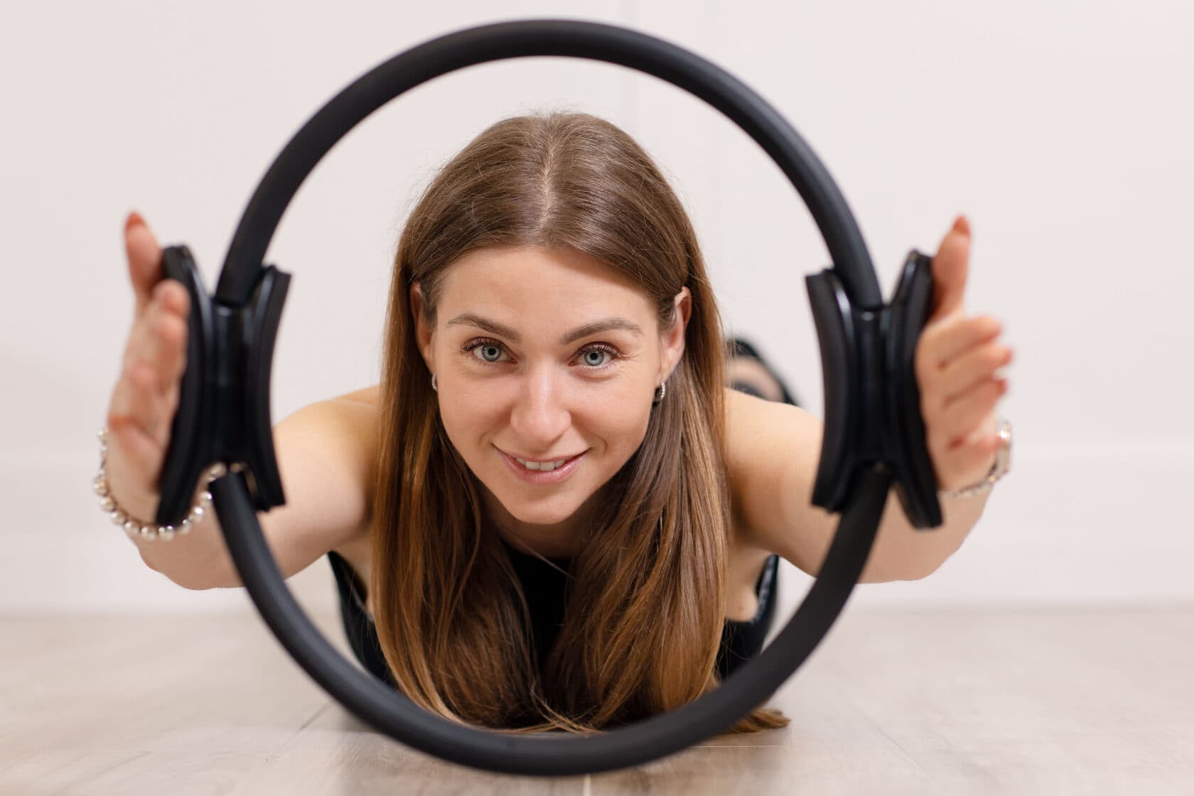 Woman smiling on a studio floor through a black Pilates magic circle